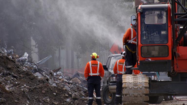 Emergency response personnel stand by a truck spraying water on rubble