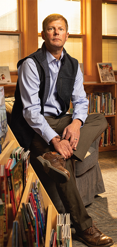 Man sits next to bookcases in a school room