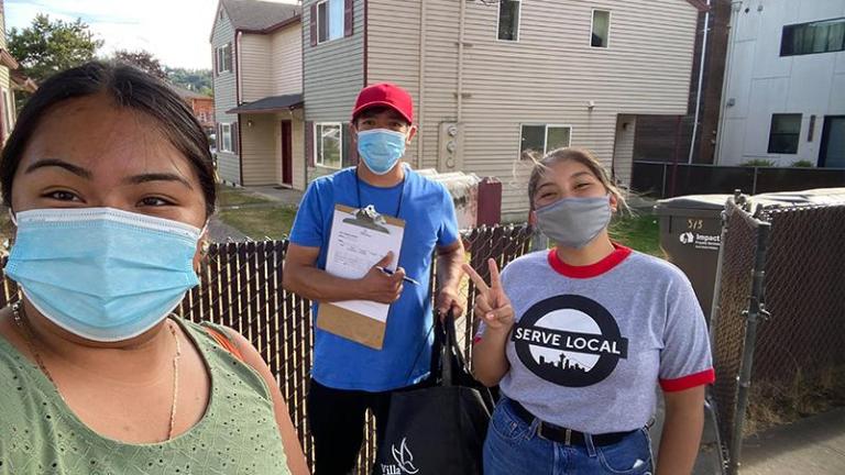 Photo of three Latinx teens wearing covid masks on a resident's porch while conducting a door to door survey 