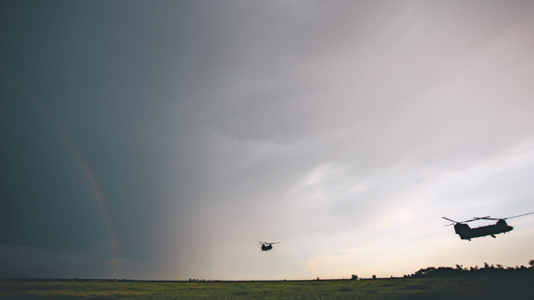 Military transport helicopter flying above a field