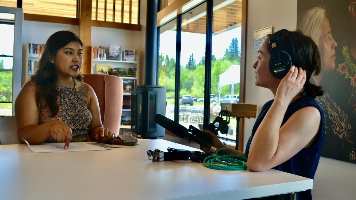 A reporter interviews a young woman in a library setting. 