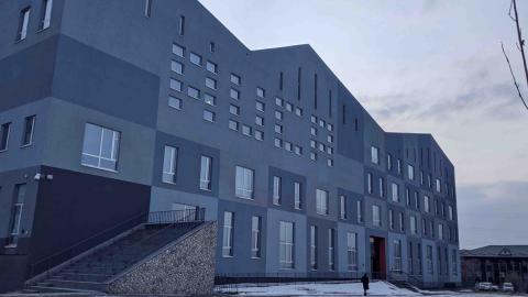 Small figure in black walking in the snow outside a gray angular building