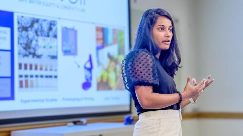 A woman presents in front of a slide. 