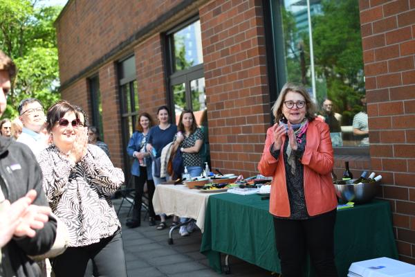 An outdoor crowd claps in front of a. table of refreshments. 
