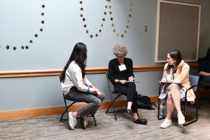 Three women in chairs confer with each other
