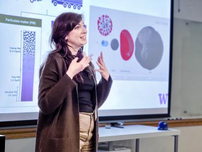 A woman presents in front of a slide.