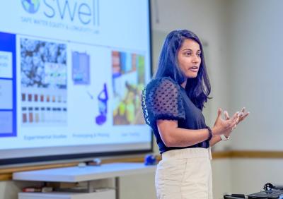 A woman presents in front of a slide on a projector.